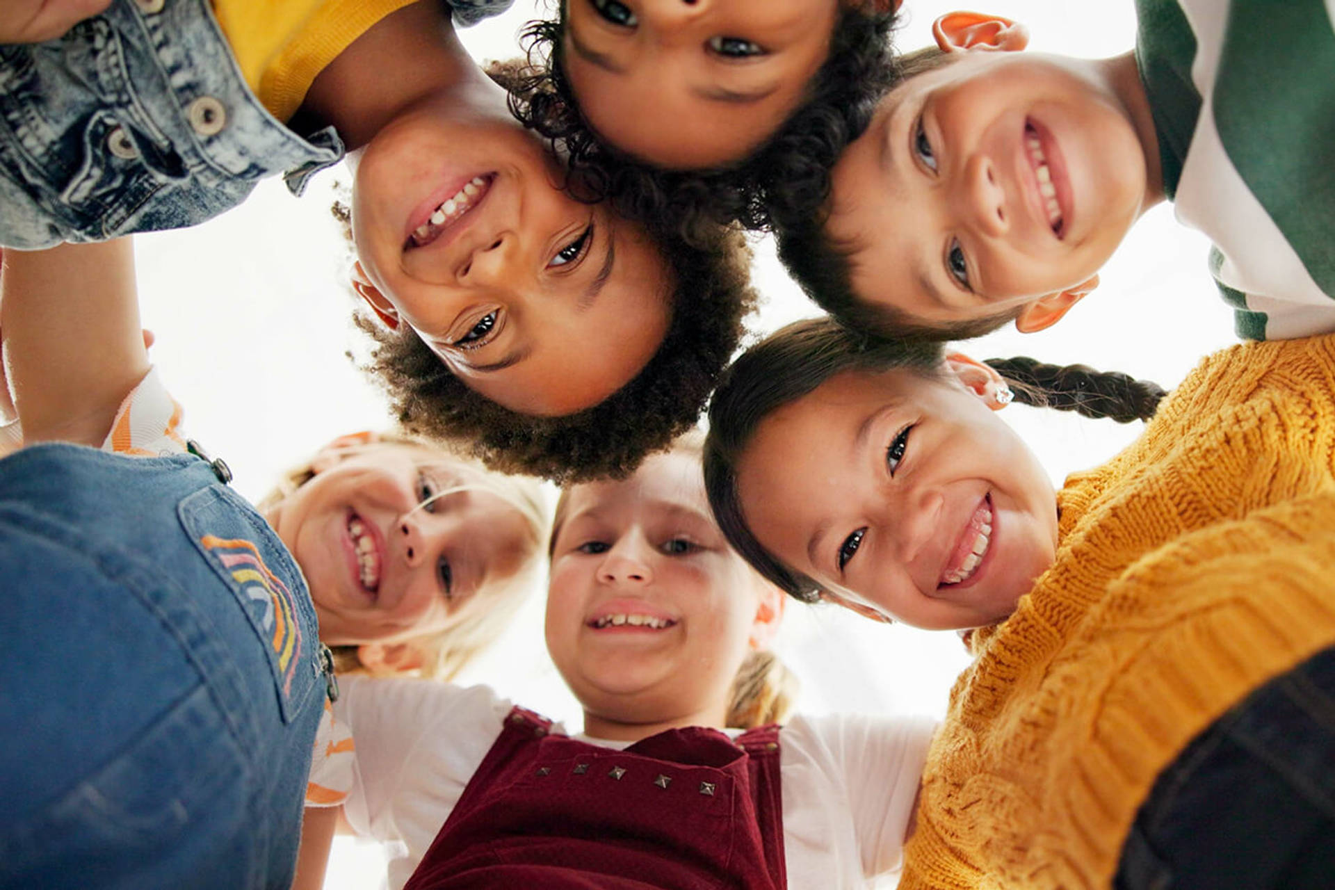 Huddle, support and happy children in school for education, community or development. Low angle, diversity and group of friends with smile in playground for solidarity, teamwork or playing together