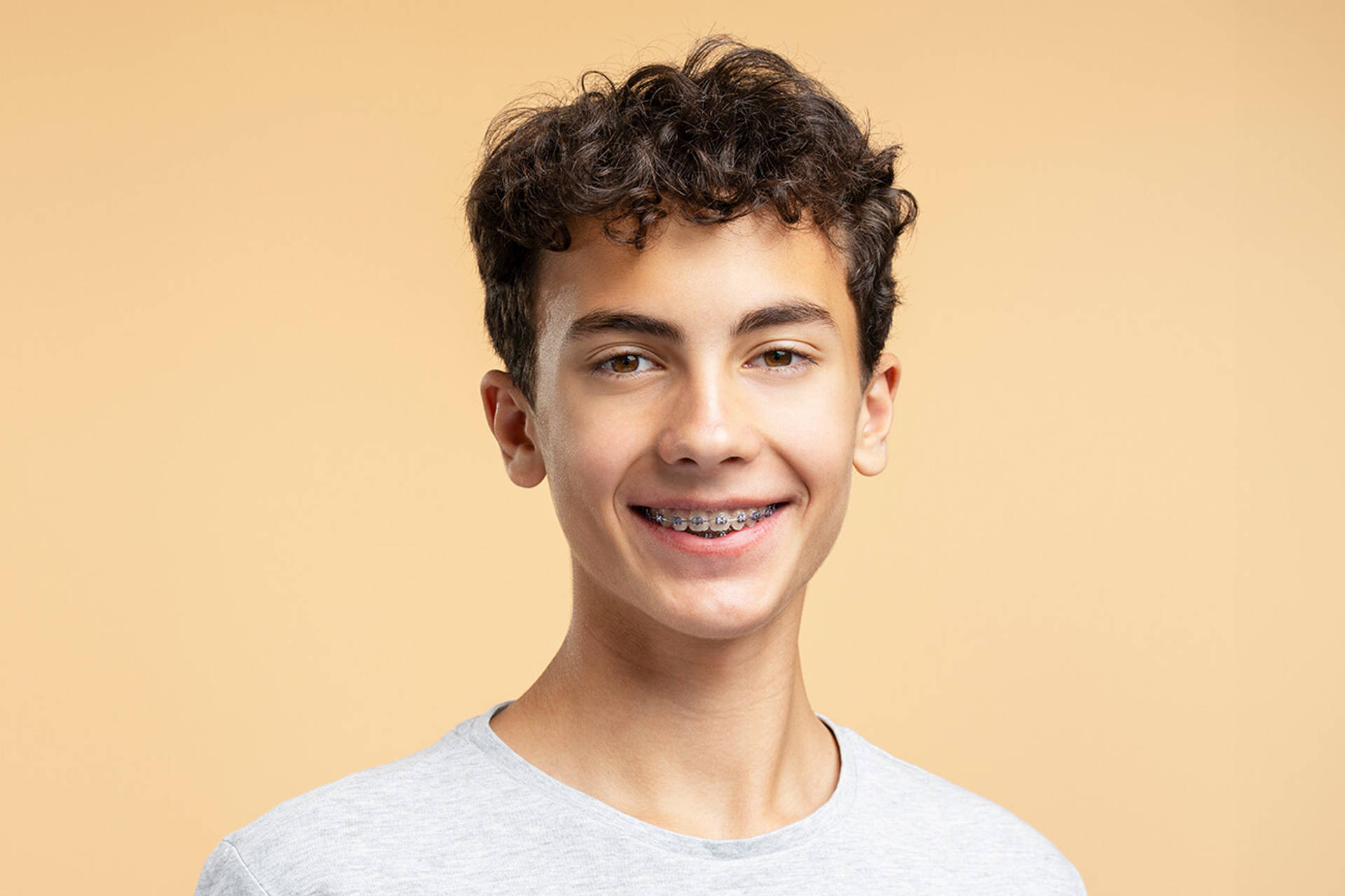 Portrait of smiling handsome boy with braces looking at camera posing isolated on beige background