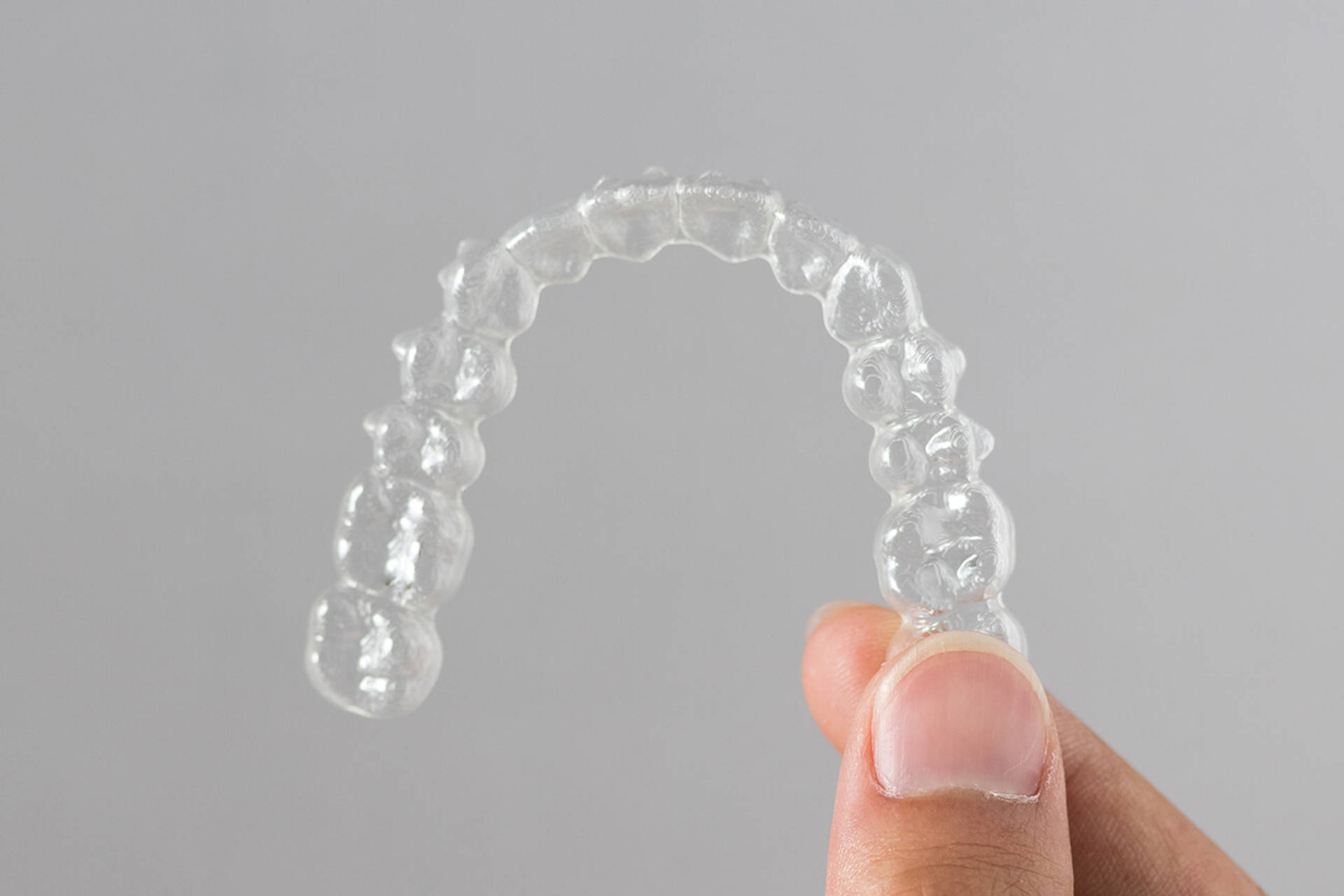 Holding invisalign braces or invisible retainers on grey background, new orthodontic equipment