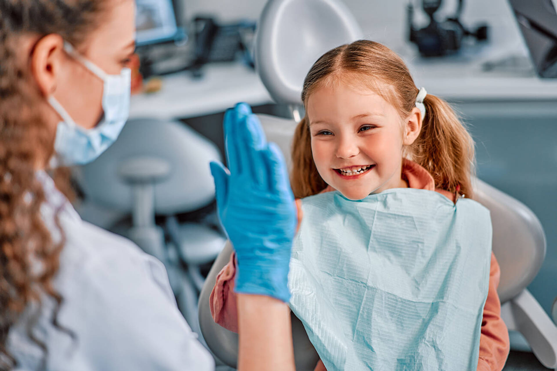 Children's dentistry. The child sits in the dental chair and cheerfully gives a high five to the nurse.