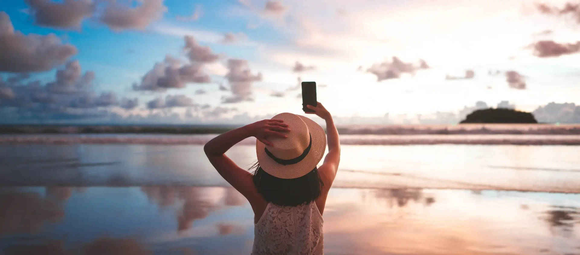 woman holding up phone at beach at sunset