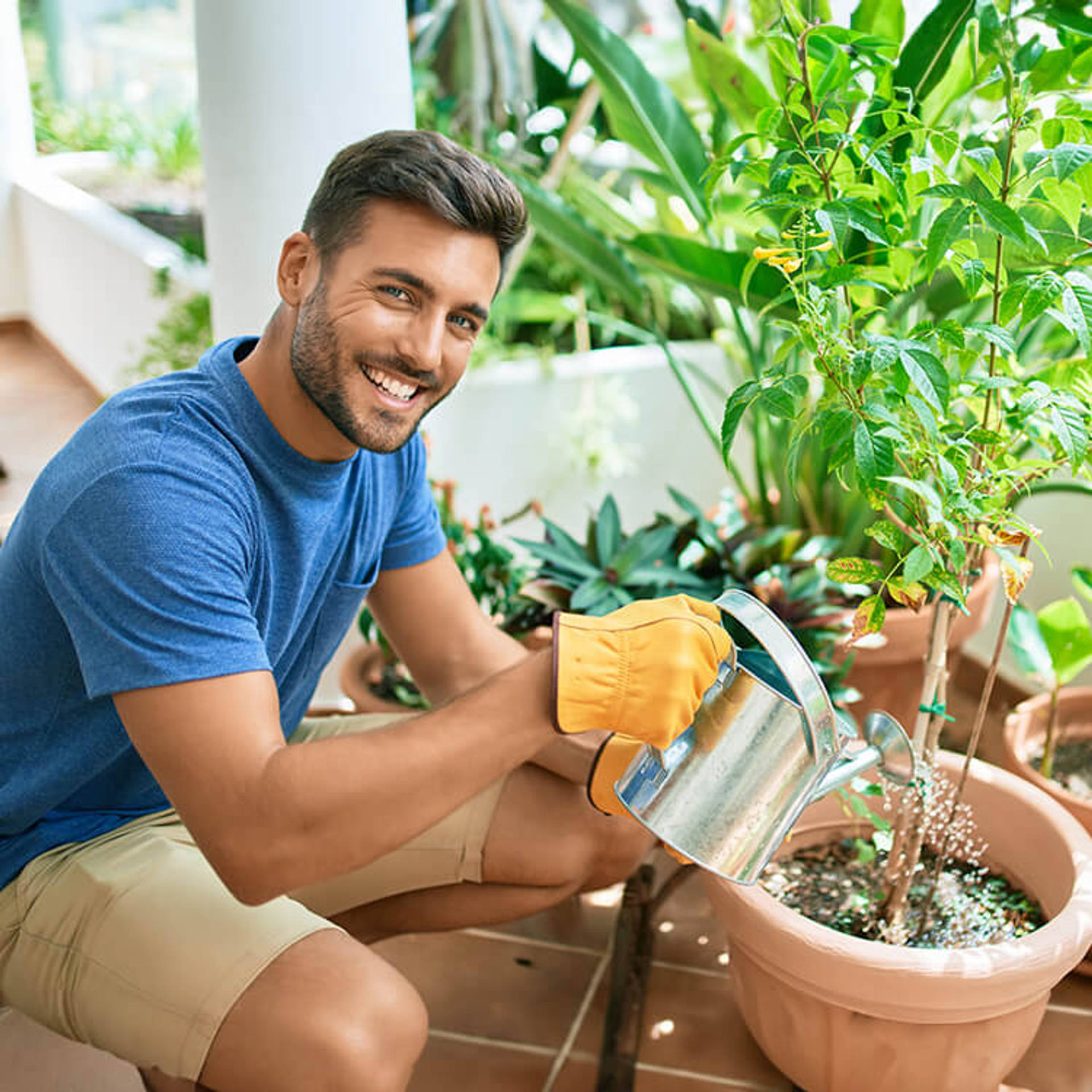 Young handsome man smiling happy caring plants using watering can at terrace