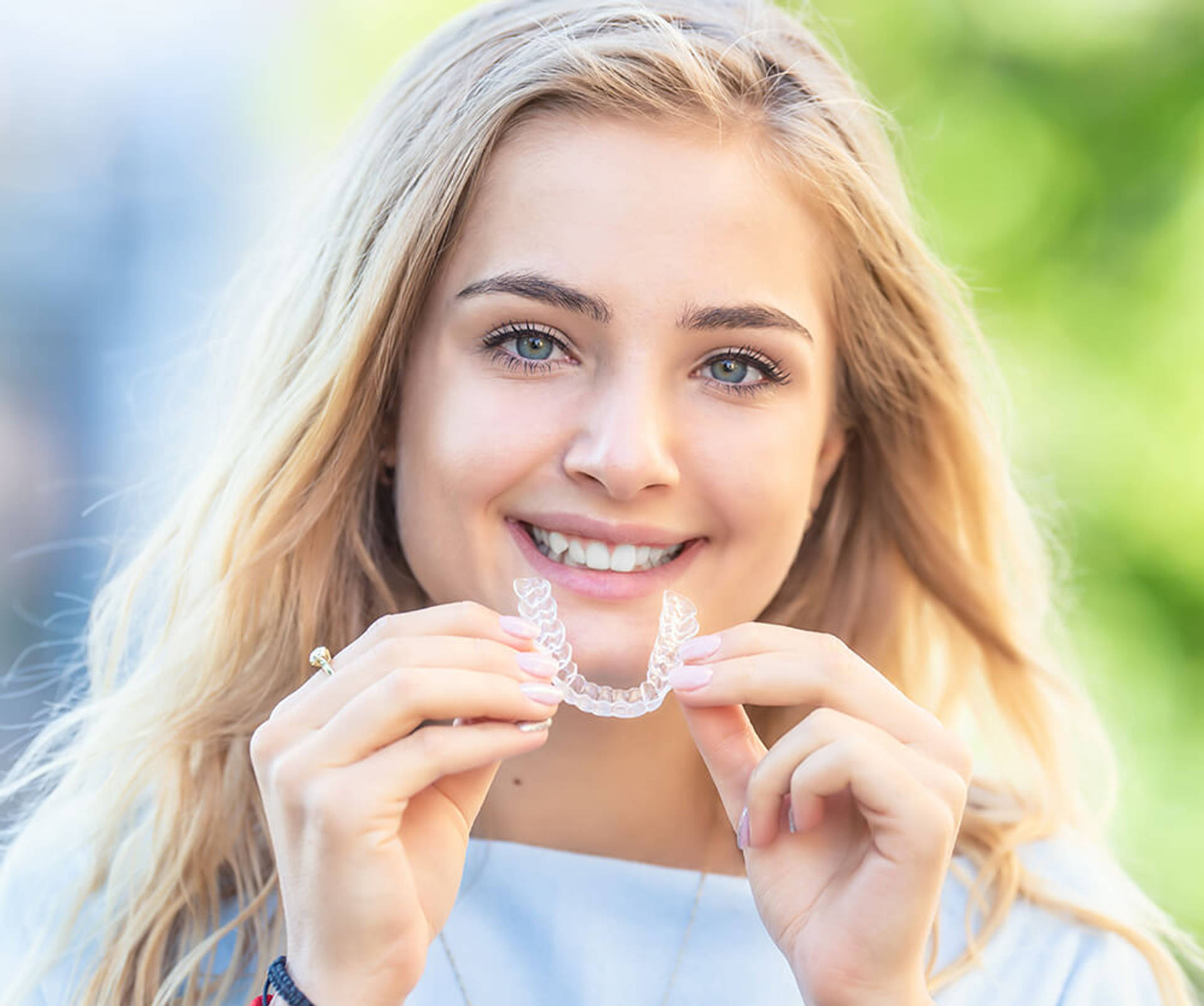 a smiling teen girl holding a clear aligner