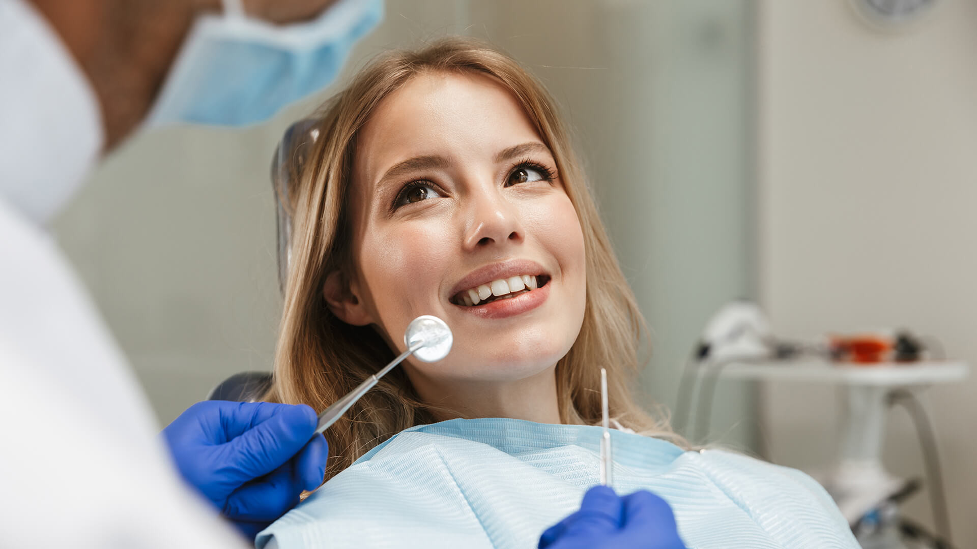 Image of smiling woman sitting in dental chair while professional doctor fixing her teeth