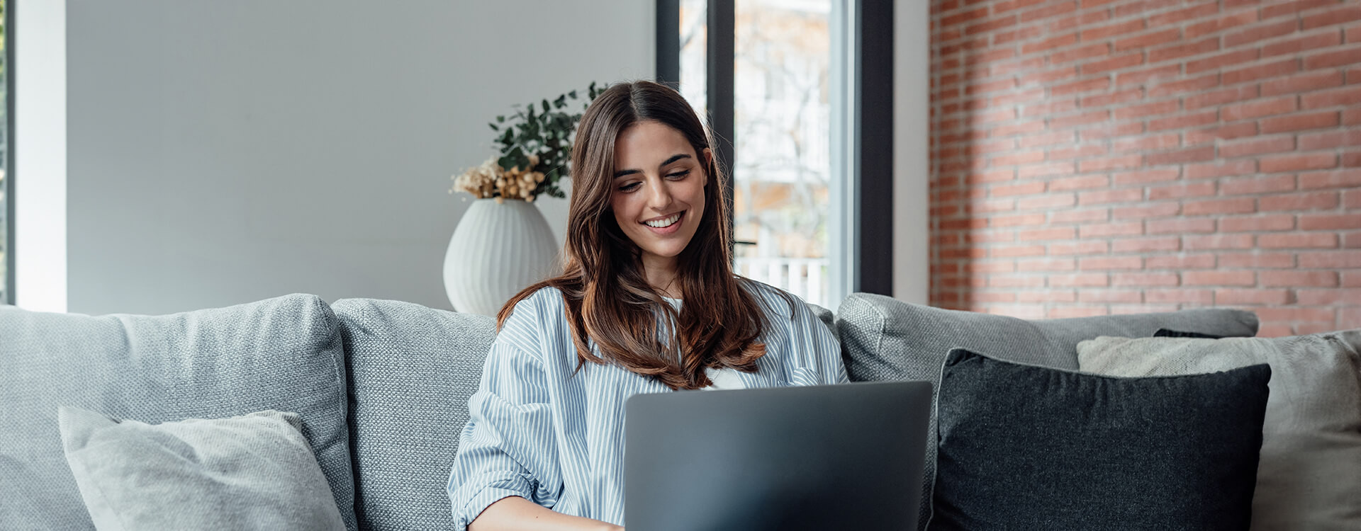 Concentrated millennial girl sit on couch working on laptop browsing internet at home during lazy weekend, focused young woman freelancer busy using computer surfing wireless web shopping online.