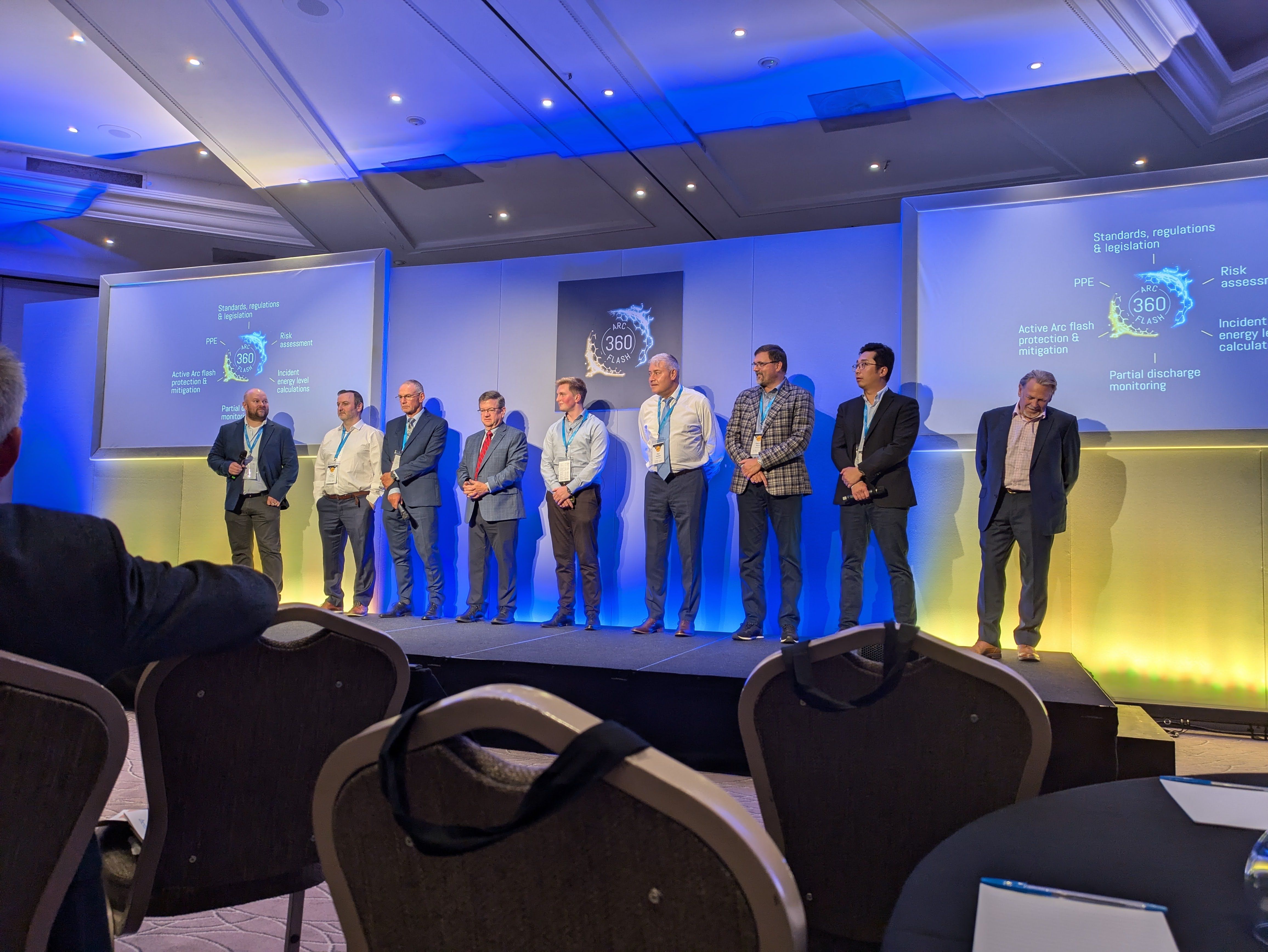 The speakers at the 2024 All About Arc Flash Conference standing on stage to receive audience applause