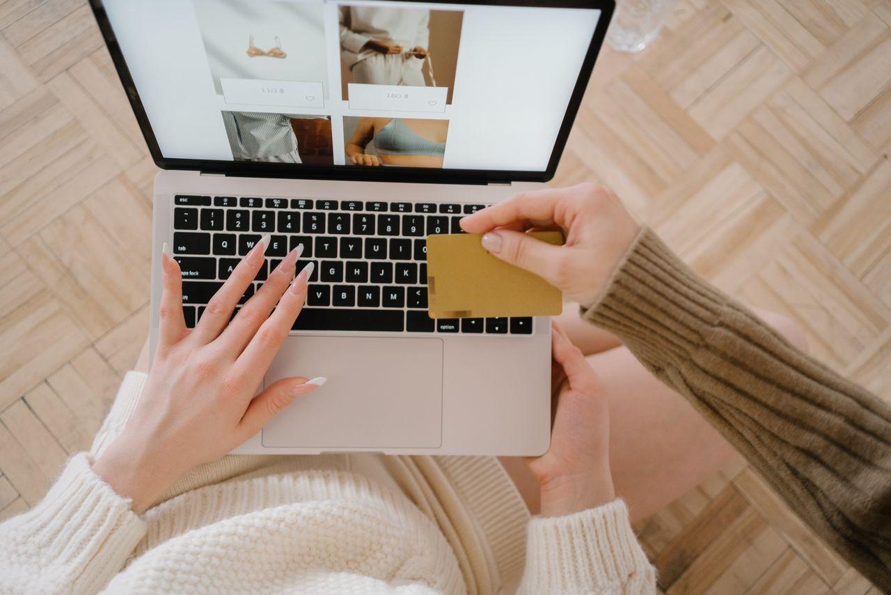 A woman makes an online purchase using a credit card on her laptop, browsing an online fashion store.