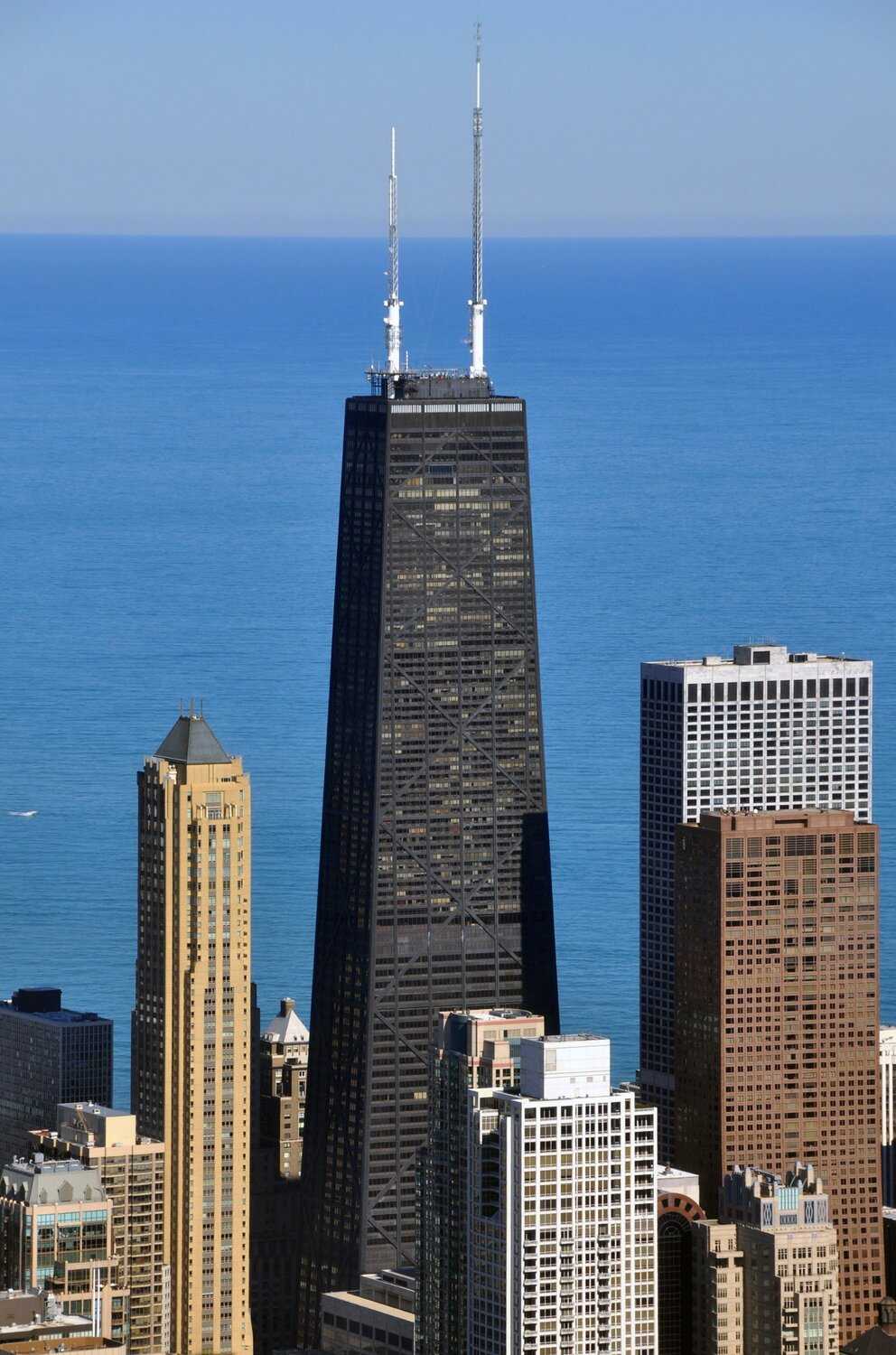 Aerial shot of 875. North Michigan Avenue, a black mid-century modern building with two tall white antennas, surrounded by other builings 