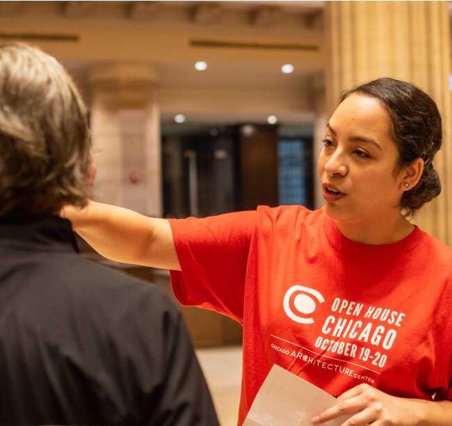 A person in a red tshirt talks to a grey haired person who is facing away from the camera