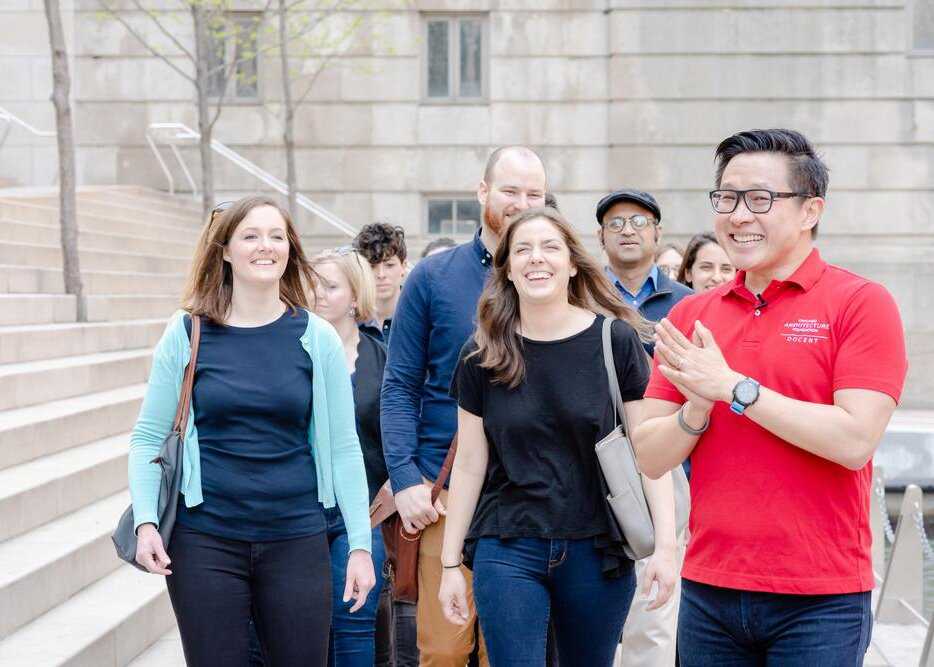 A docent smiling and leading a group of tourists in a city