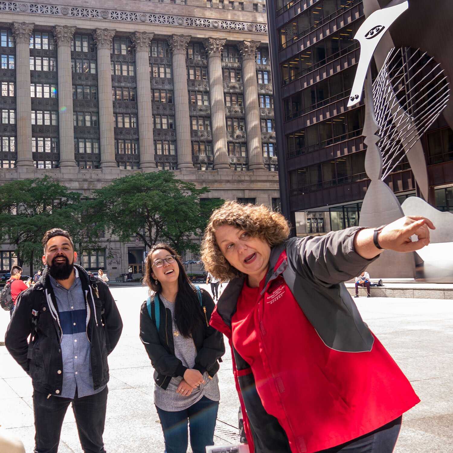 Photo courtesy of CAC/ Anna MunzesheimerThree people on a city street. One in a red docent t-shirt is pointing off screen. 