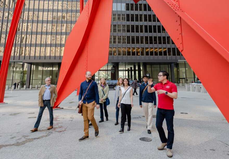 A group of people underneath a red scuplture