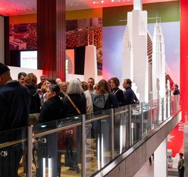 a group on an indoor balcony with a white skyscraper model in the background