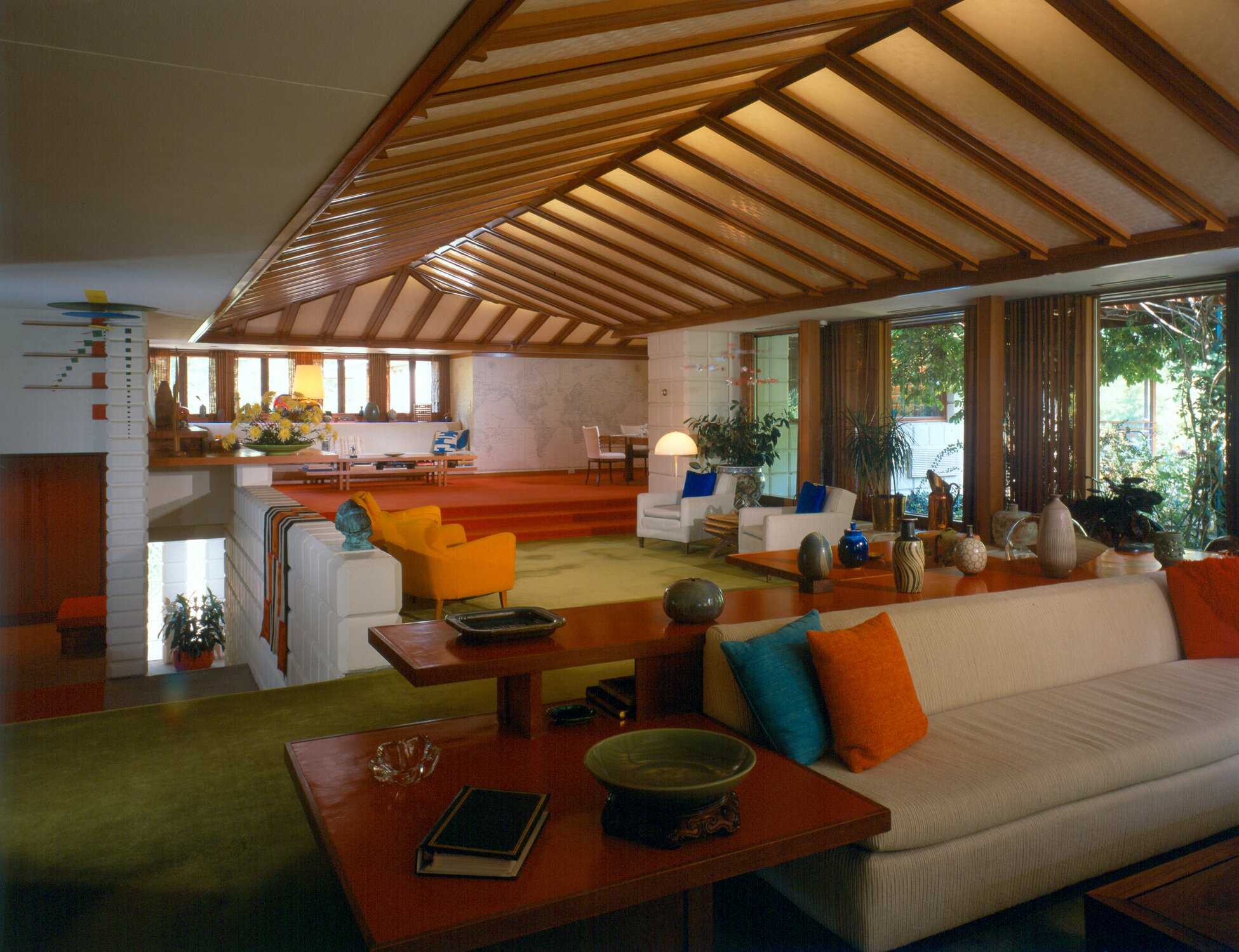 A living room with green carpet and bright colored furniture. The ceiling has wood beams.