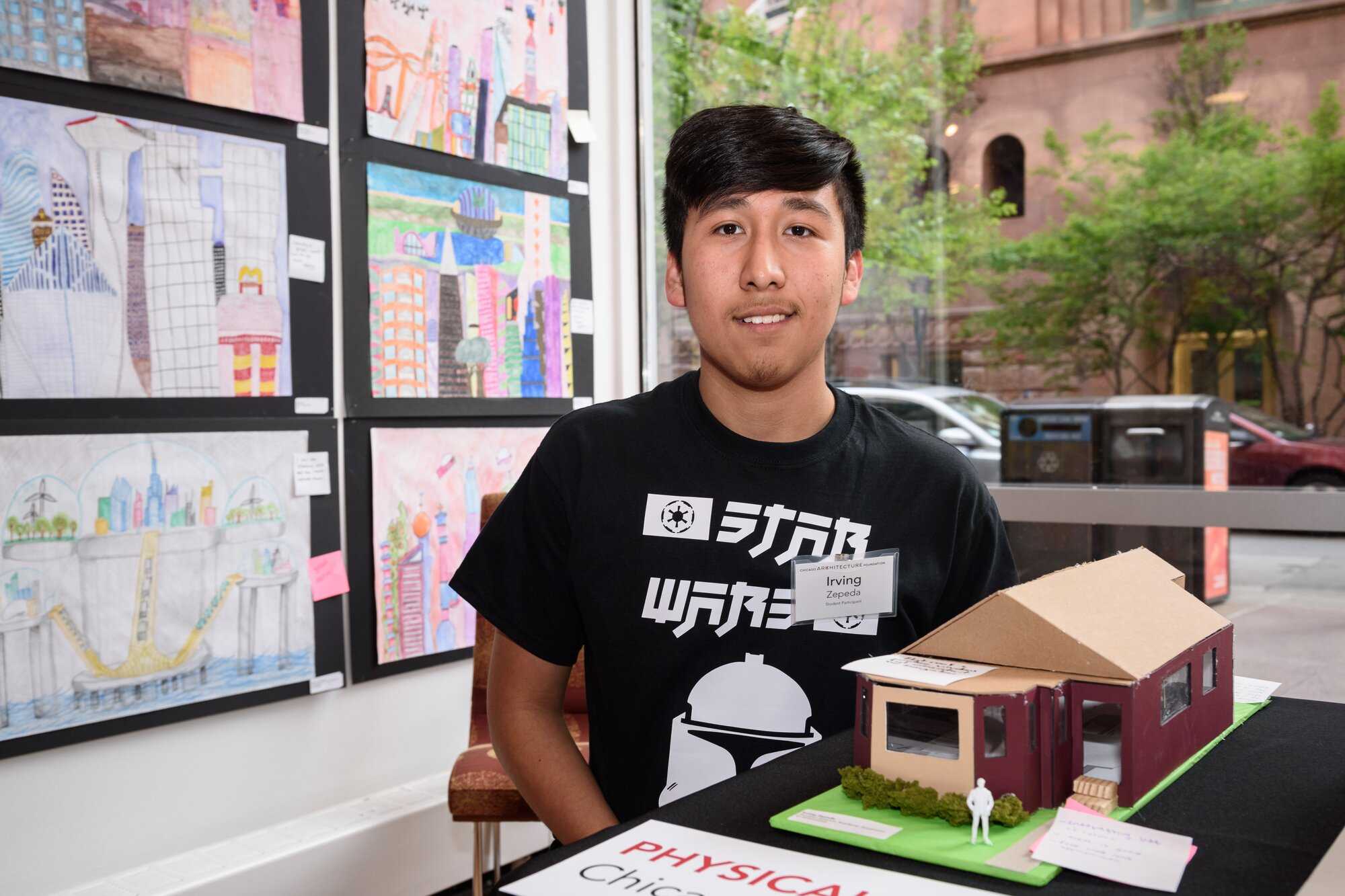 Latino teen with a black tee standing next to his build model