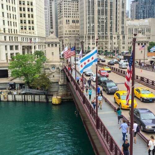 Bridge with cars, over river, with multiple flags. 