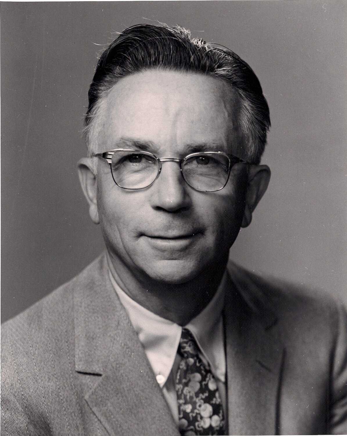 A black and white portrait photograph of a caucasian man with glasses.