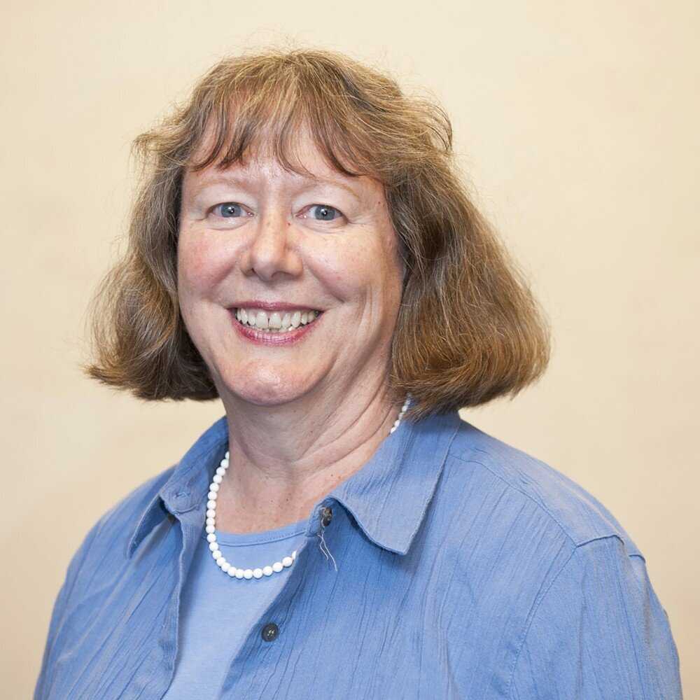 Headshot of a smiling caucasian woman with blue top and pearl necklace