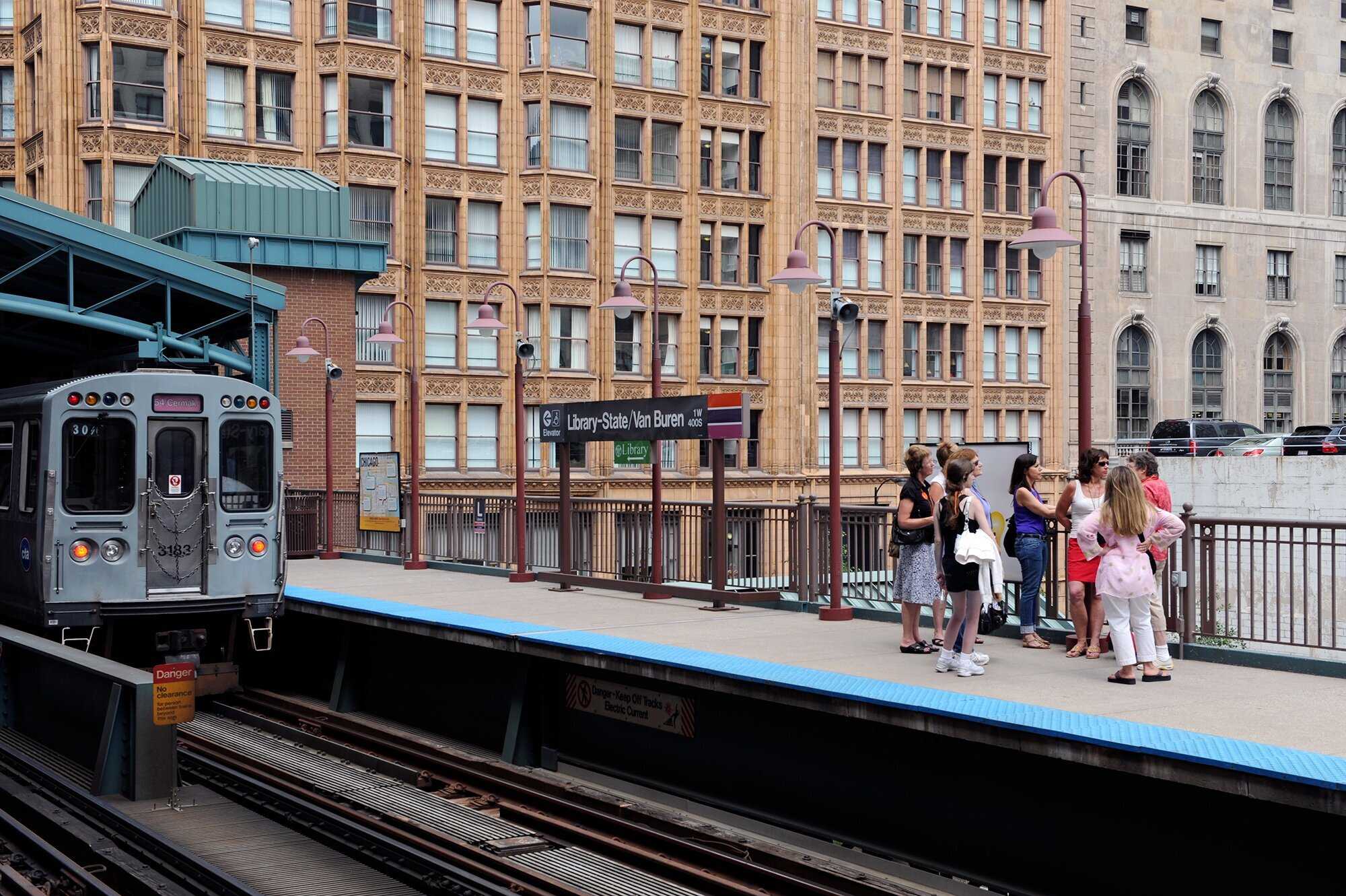 Group of people standing on elevated train platform with building in distance