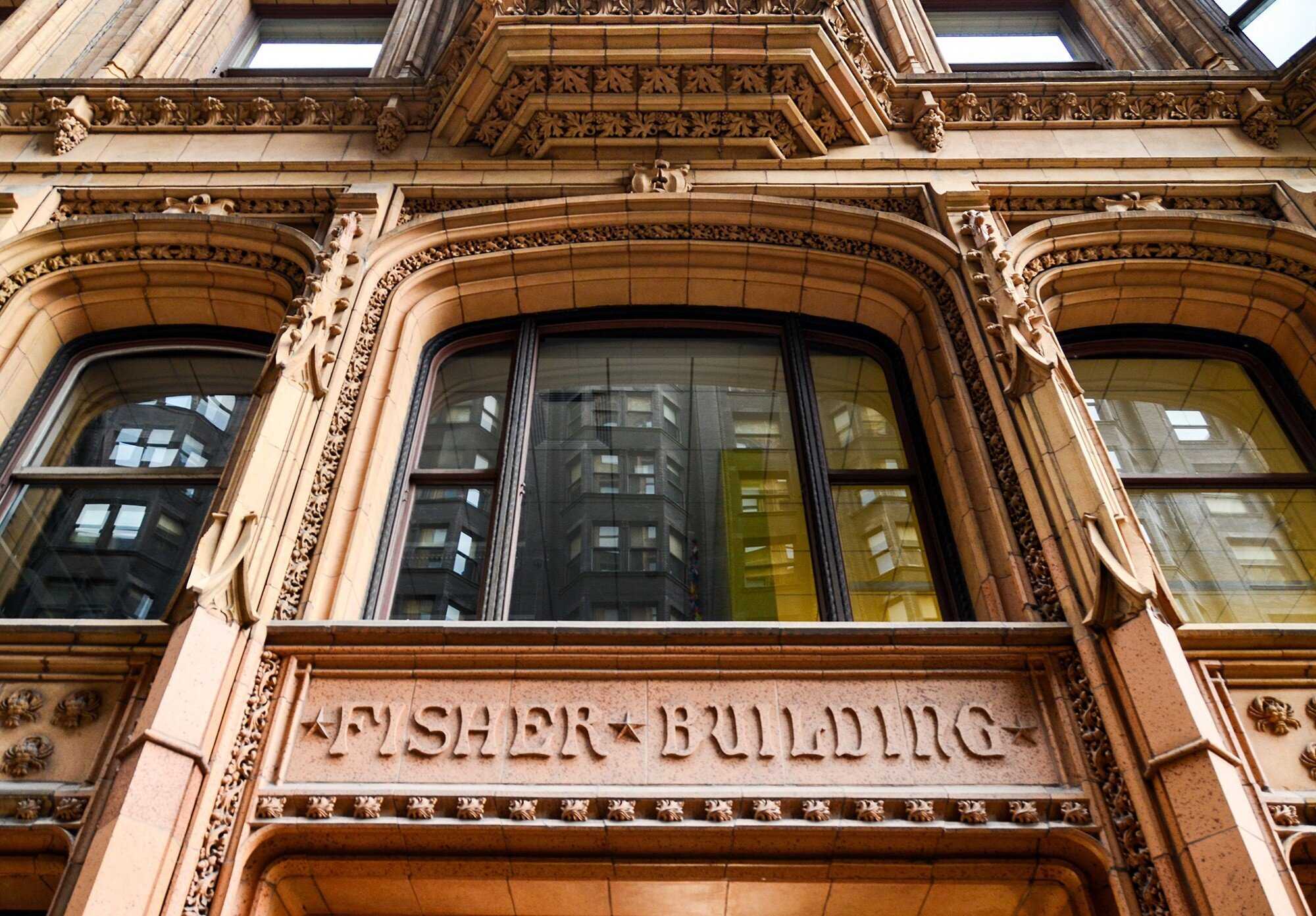 Looking up at reddish beige entrance to building with "Fisher Building" engraved over door.