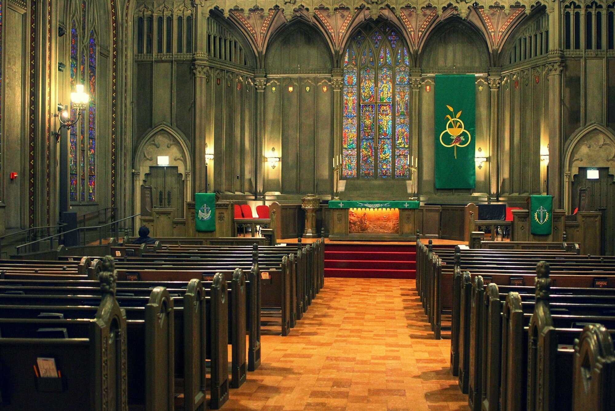 Roopm filled with wooden pews on either side and an orange tiled floor. the walls and the pews are both green 