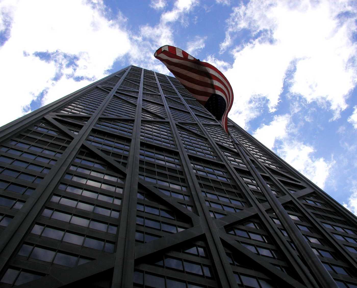 An American flag waves in front of a tall black building.