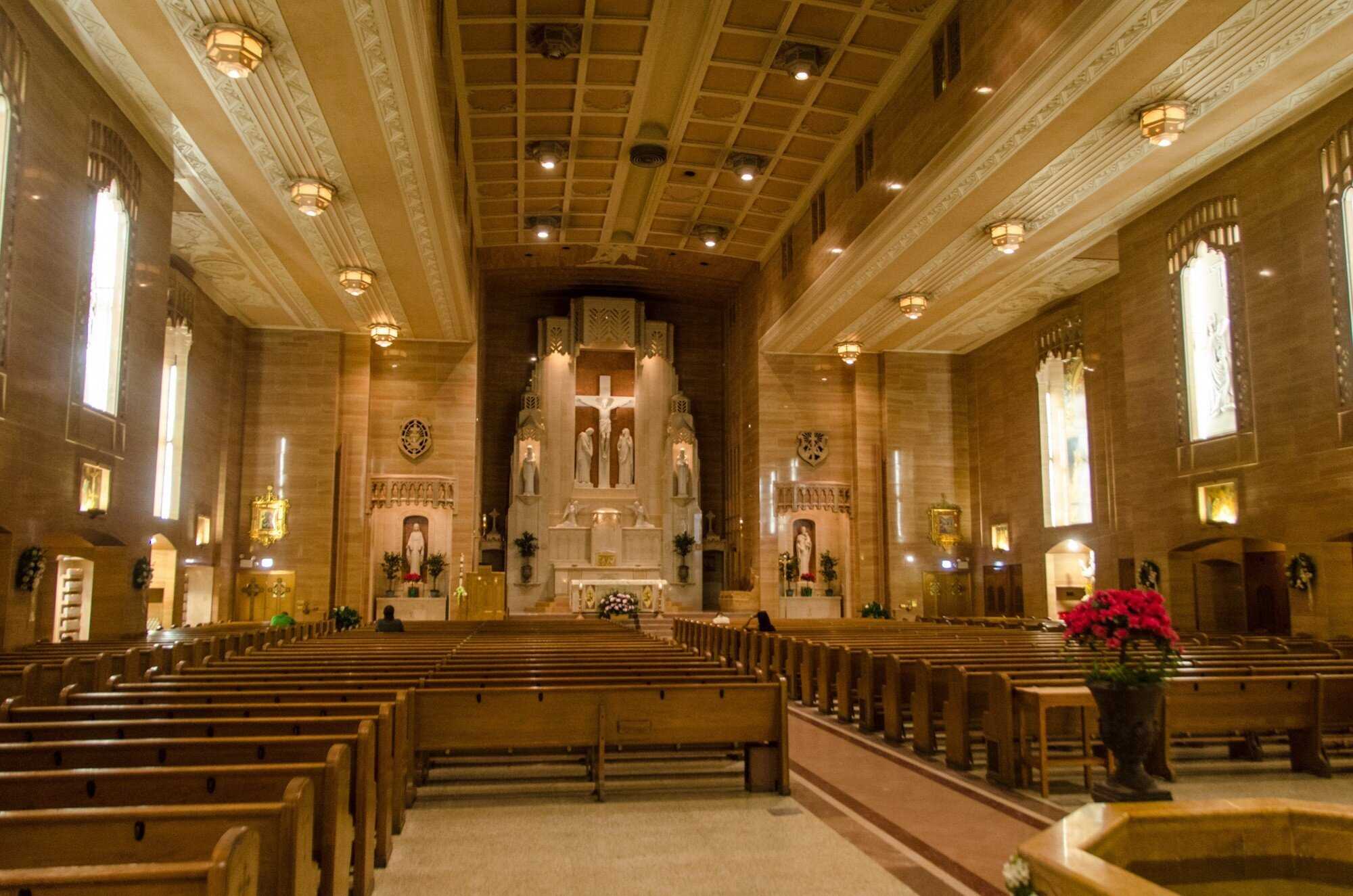 Interior of a warmly lit Catholic church with wooden pews on each side of the room