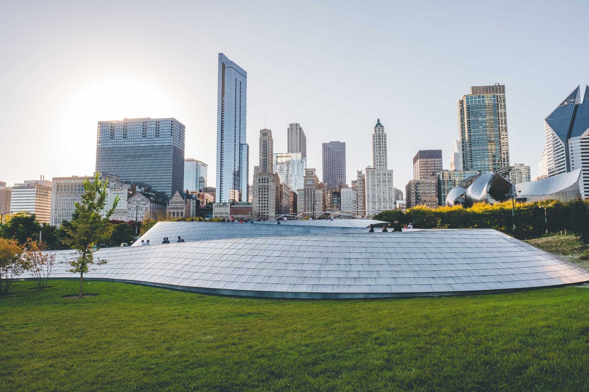 Large metal sloped structure sits on green grass with skyscrapers in the background