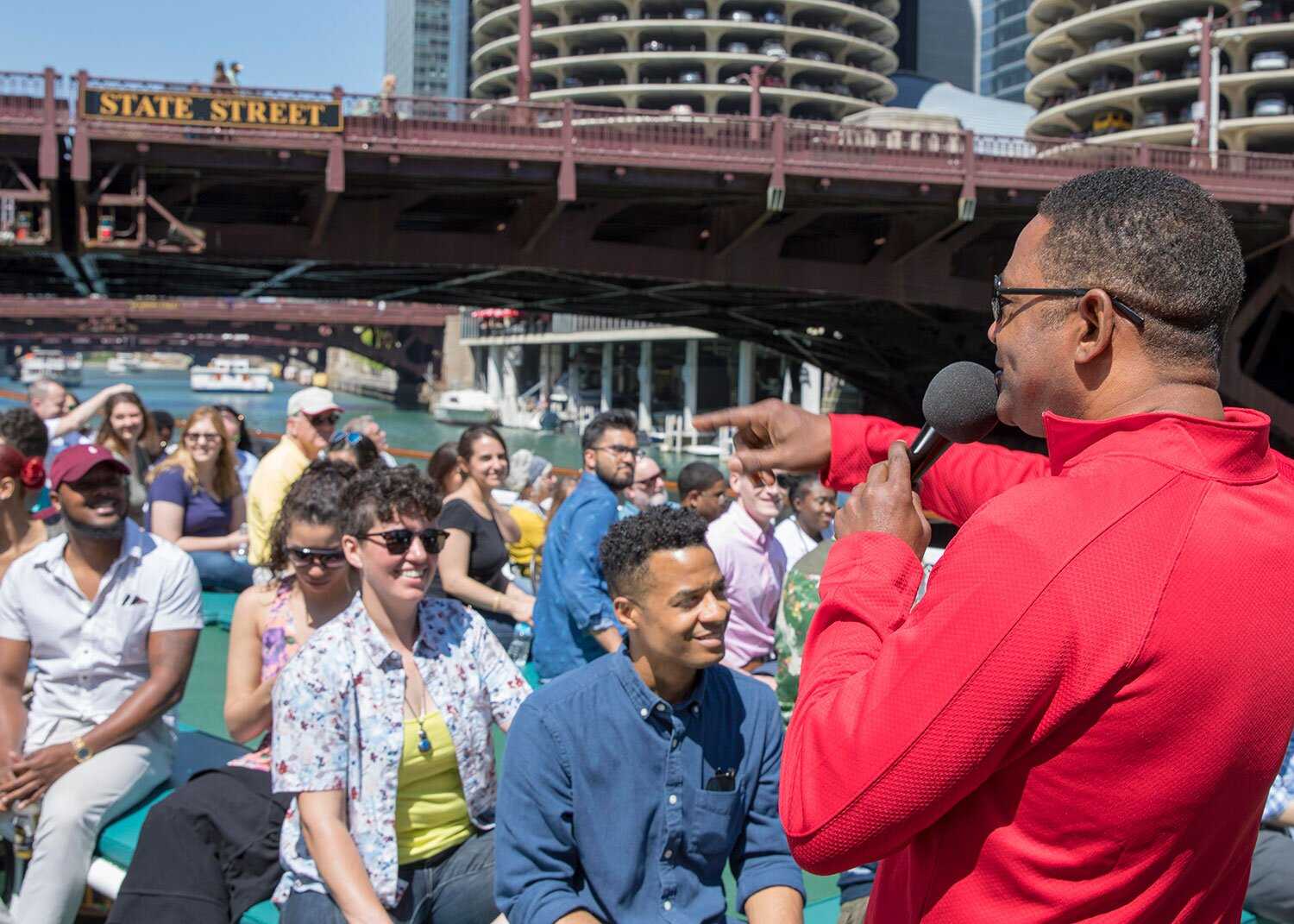 A docent in red pointing at a crowd seated on a boat tour