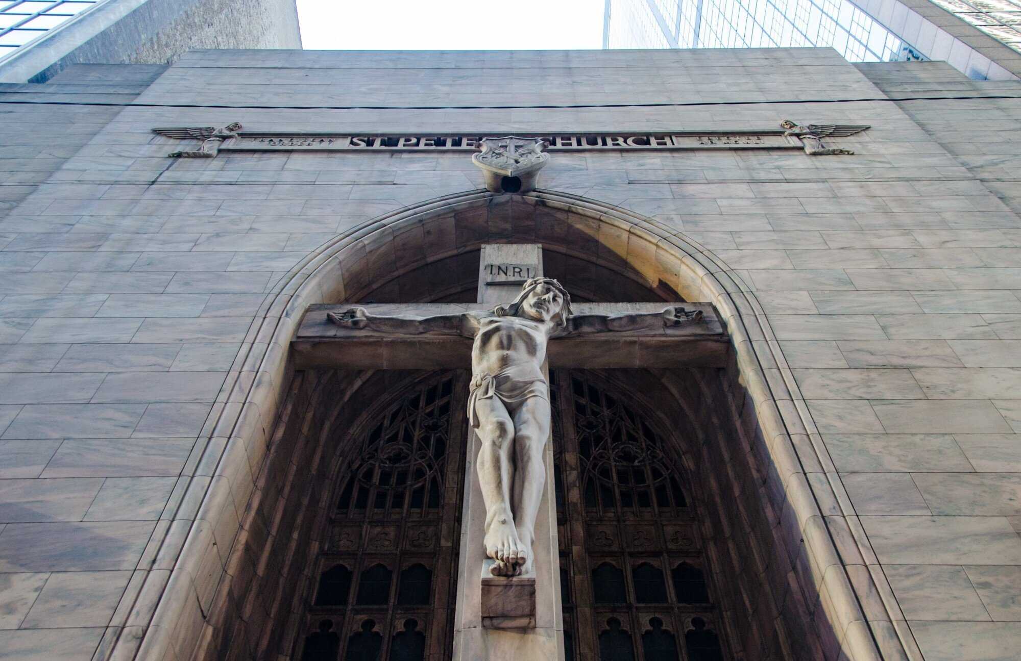 Image looking up at a sculpture carved in stone of Jesus with his arms spread across a cross