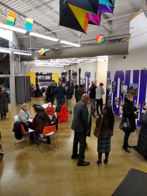 Gallery space with people standing and sitting talking to one another.