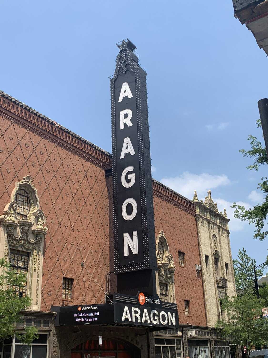 Exterior view of red brick building with diamond patterning. Large black vertical sign.