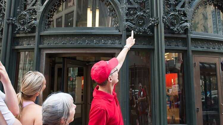 man in red shirt and red cap pointing up at building feature 