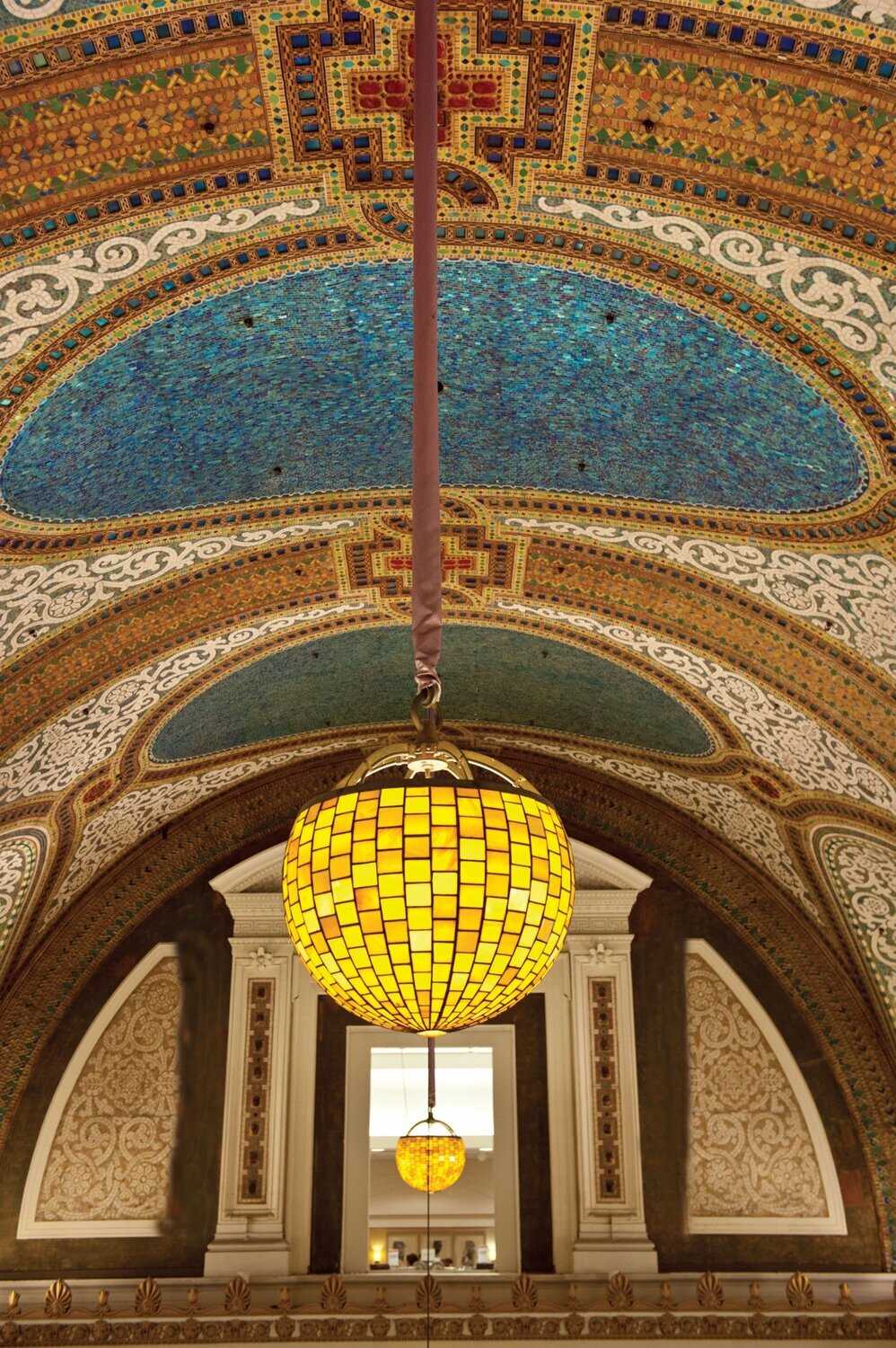 Yellow golden globe light fixture hanging from mosaic glass ceiling.