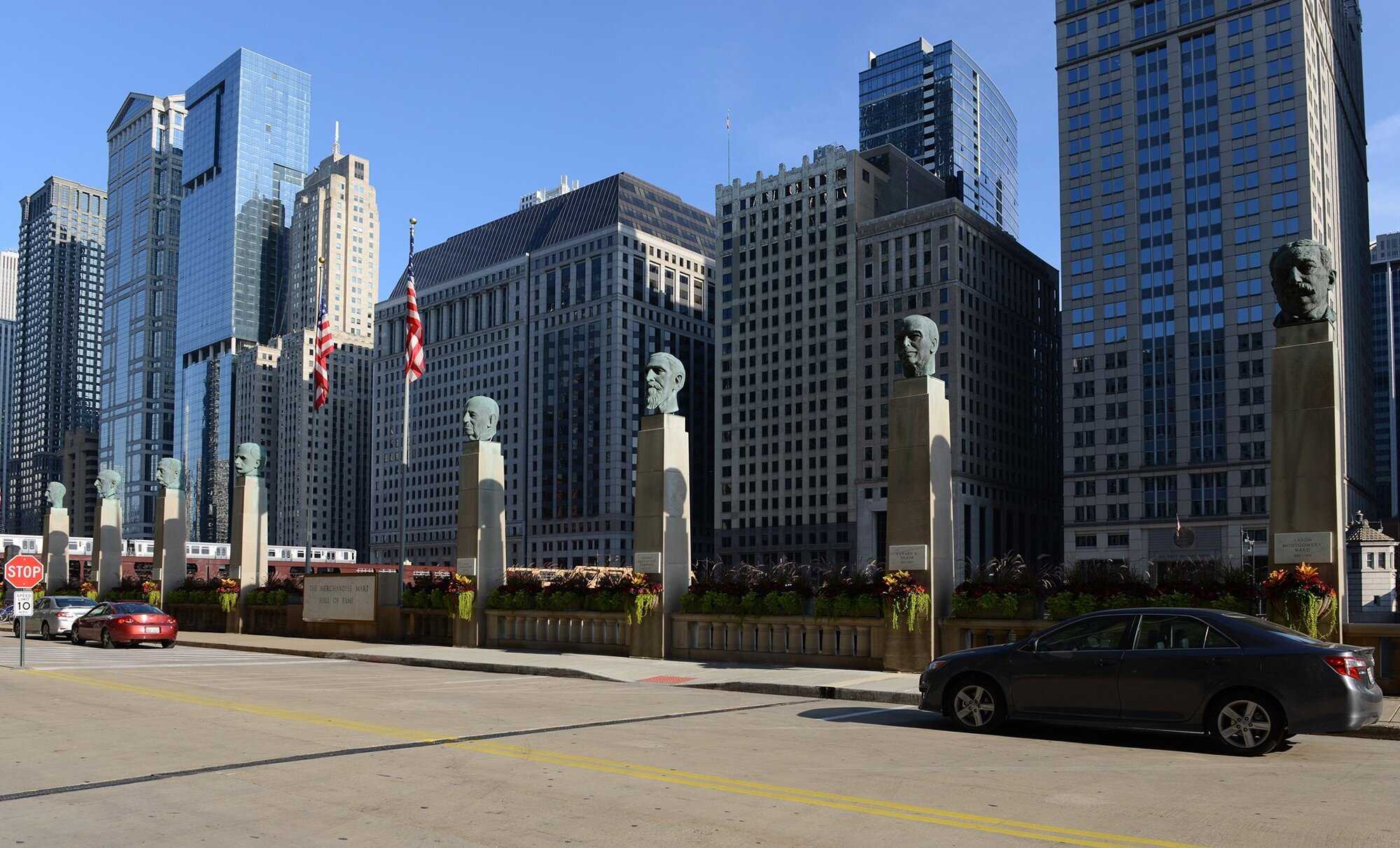 Row of busts on pillars along sidewalk by river