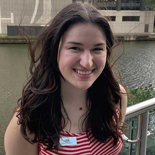 Caucasian woman in her early twenties, smiling, in a red and white striped tank top standing in front of the Chicago river.