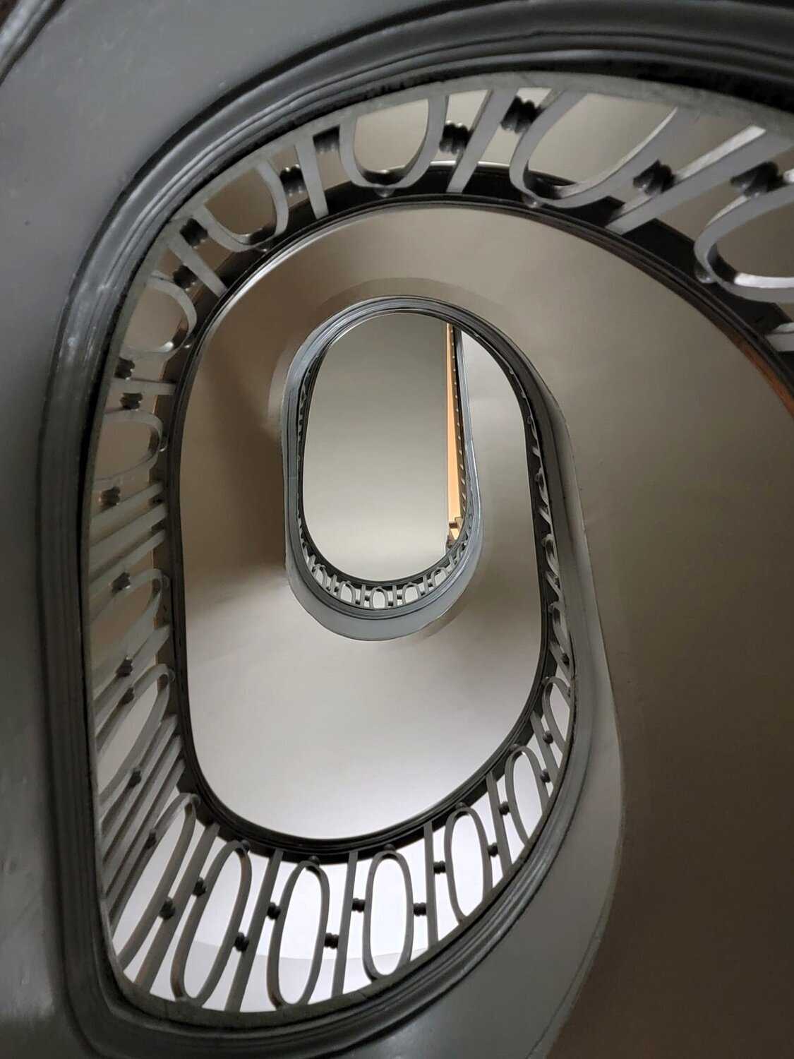 Looking up through oval-shaped multi-level stairwell with dark wood banisters