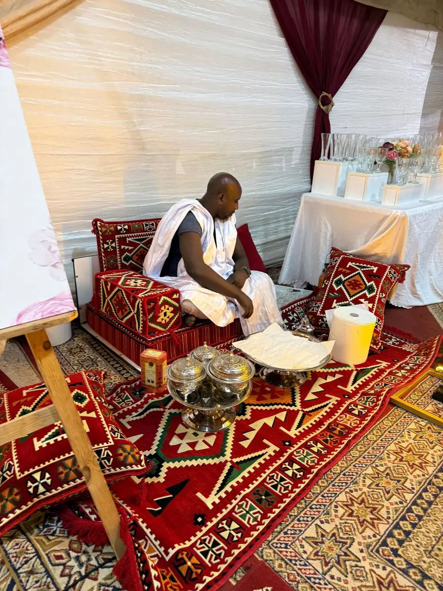 Man in a derraa sitting on a red Sahrawi majlis in front of a tea tray