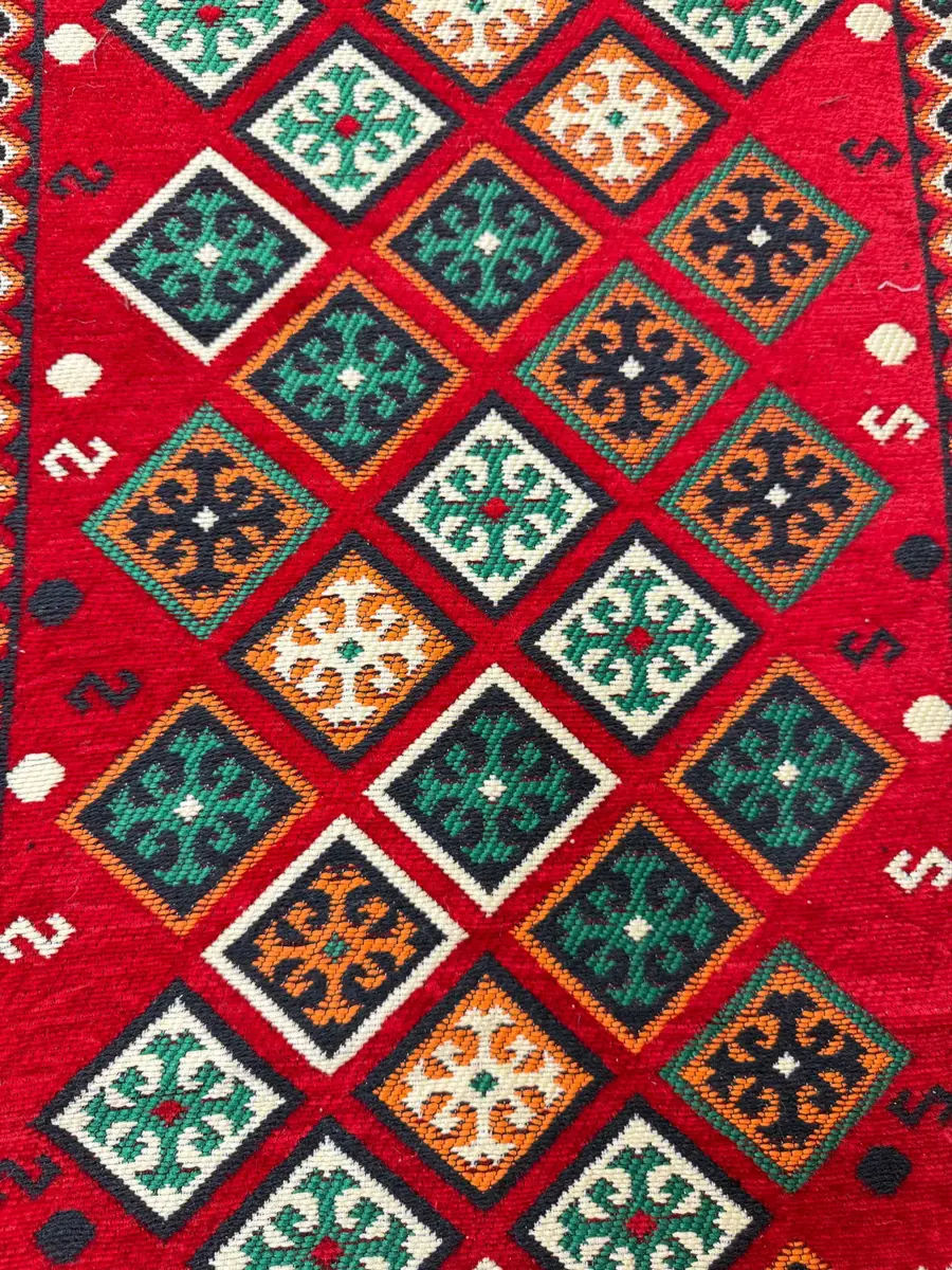 Gros plan sur un tissu de majlis sahraoui rouge à motifs géométriques verts, orange et blancs