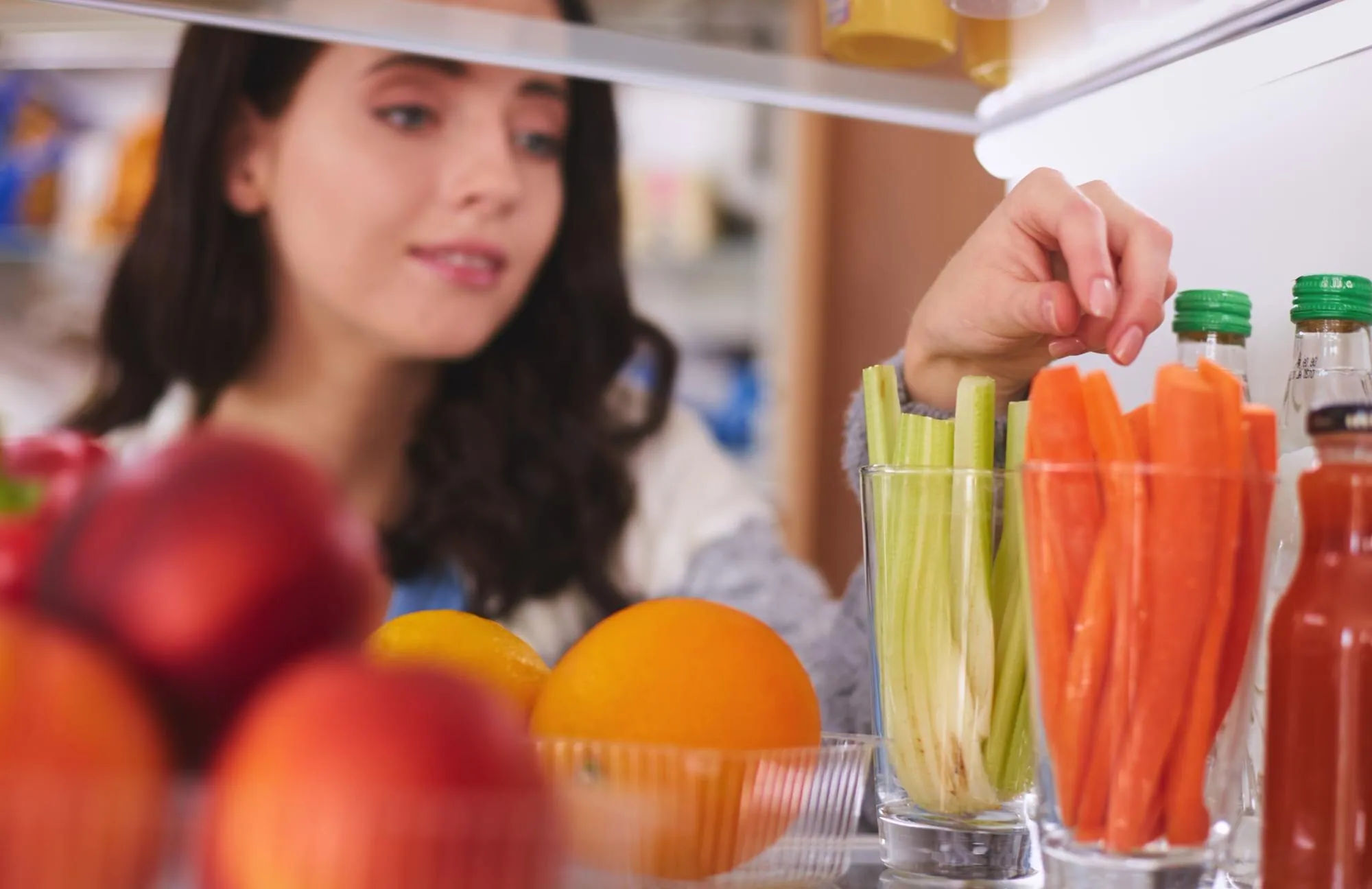 Person checking fresh food in an open refrigerator before grocery shopping