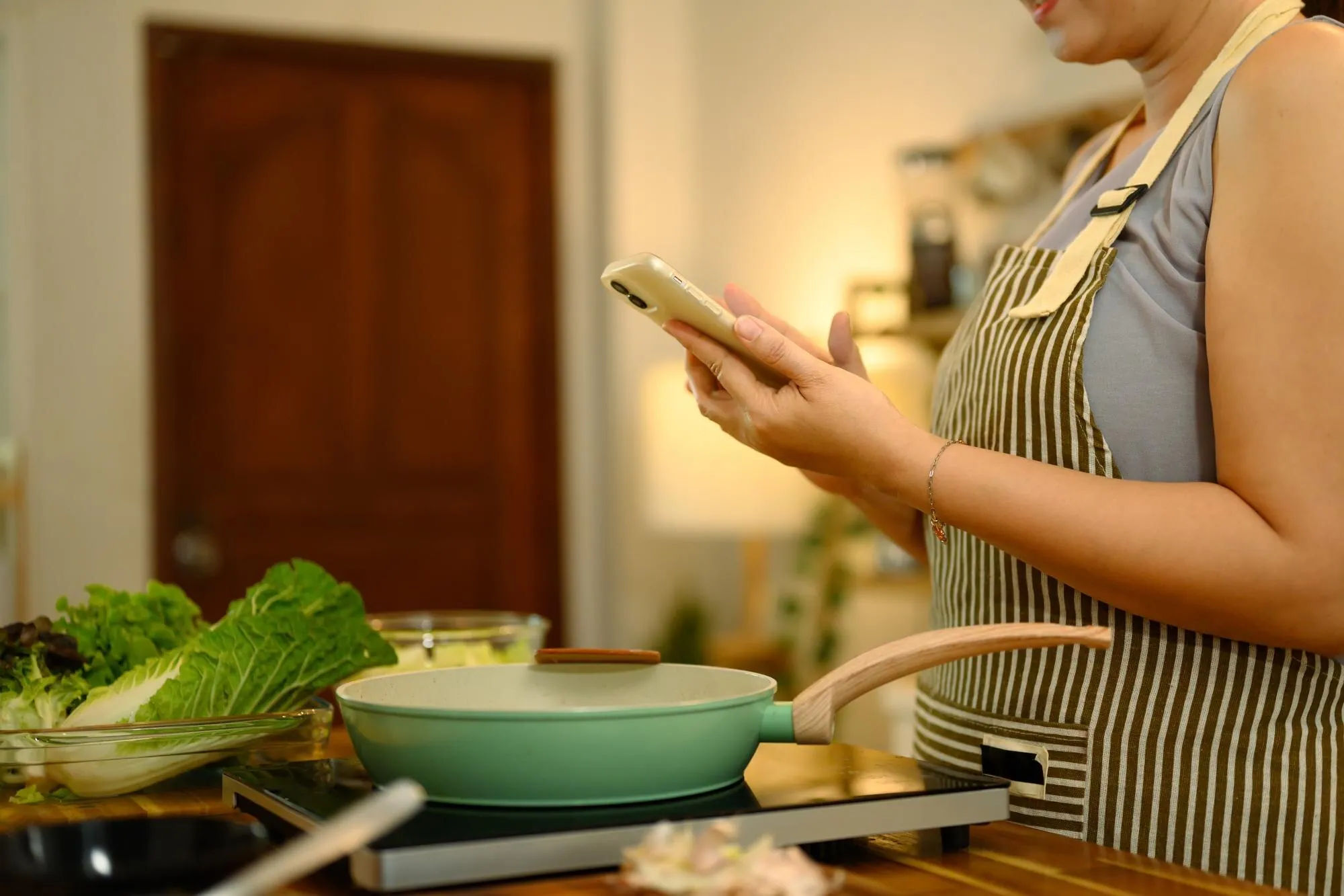 Home cook checking a saved recipe while preparing vegetables at the stove