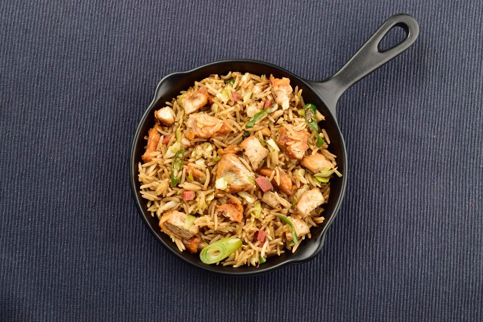 Arroz salteado con pollo y verduras en una sartén oscura