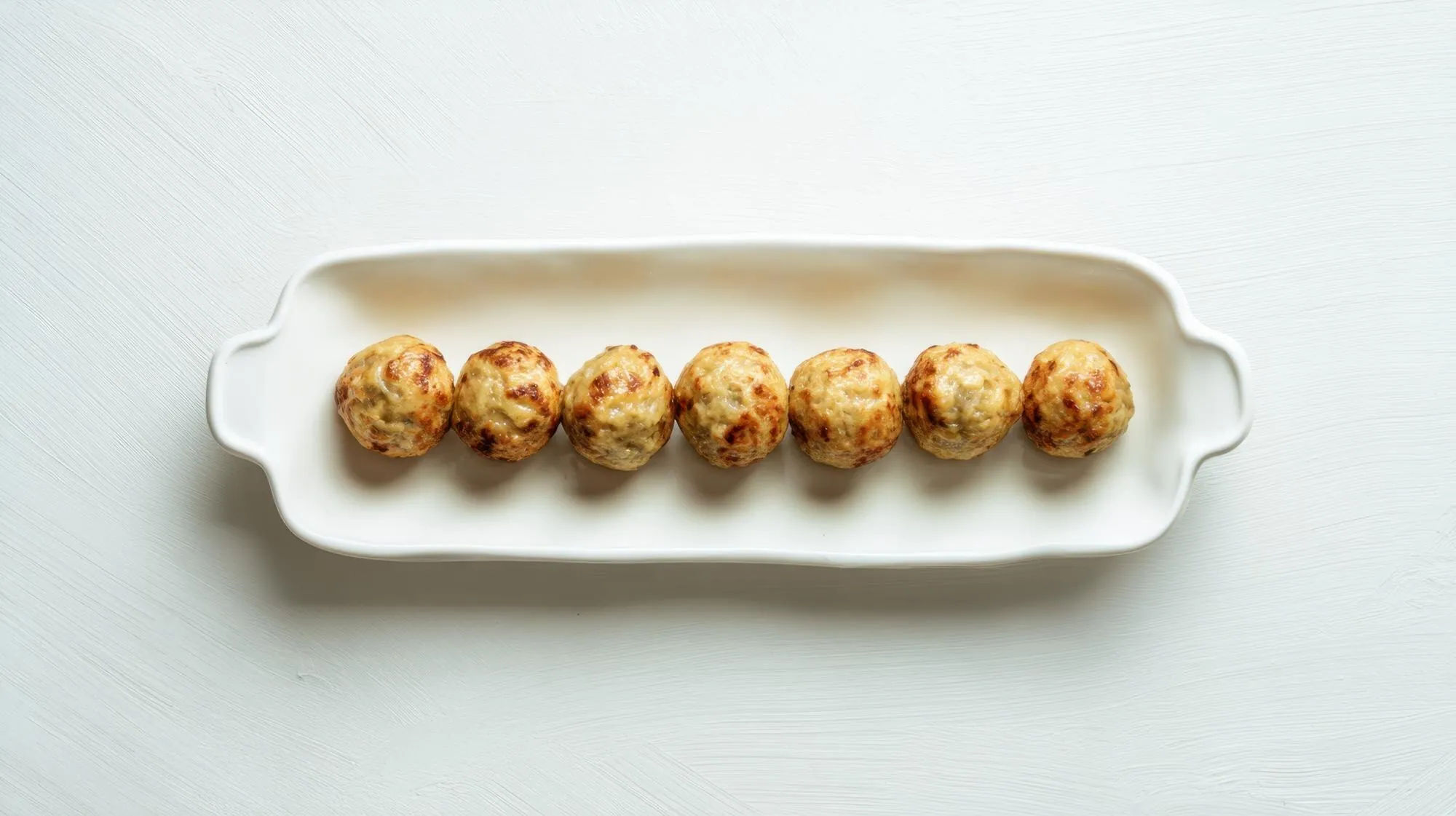 Golden party meatballs arranged on a white serving platter