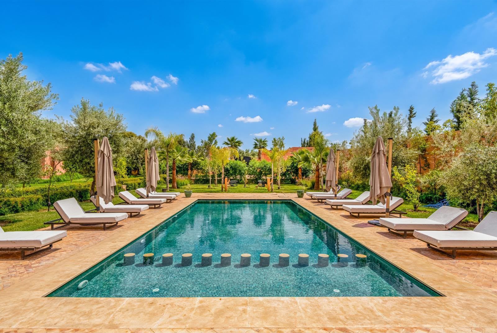 Grande piscine extérieure du complexe de Pilates à Marrakech, entourée de verdure luxuriante