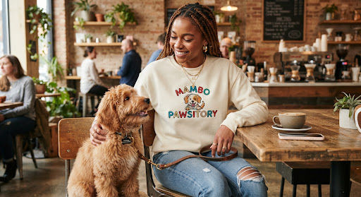 Woman with her dog wearing Mambo Pawsitory sweatshirt in a cafe