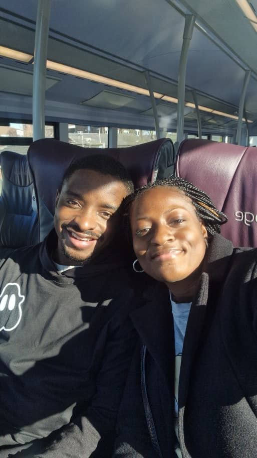 Mary and Paul leaning together in coach seats, wrapped up in dark coats.
