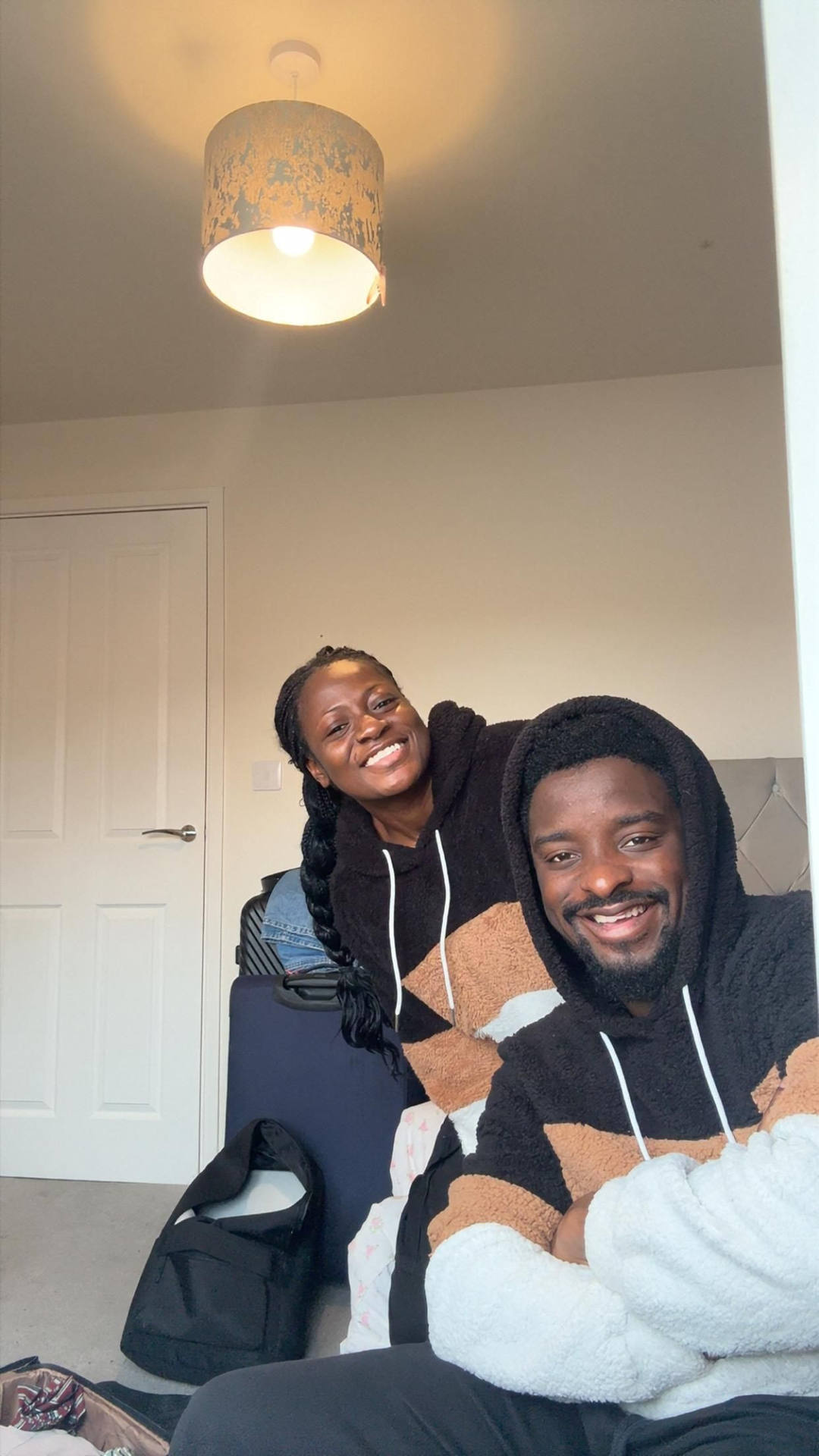 Mary and Paul in matching fleece hoodies in a bedroom, a packed suitcase behind them.