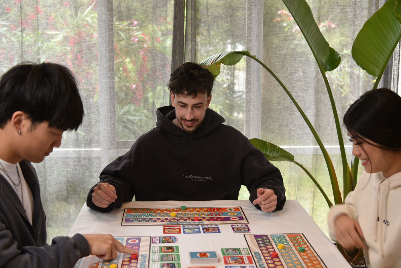 Three players at a table mid-game, life tracker boards and cards spread out
