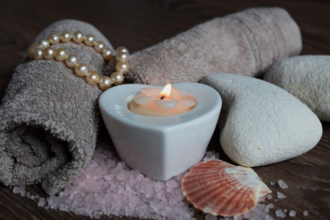 Image of warm towels, stones, shells and salt on a spa table.