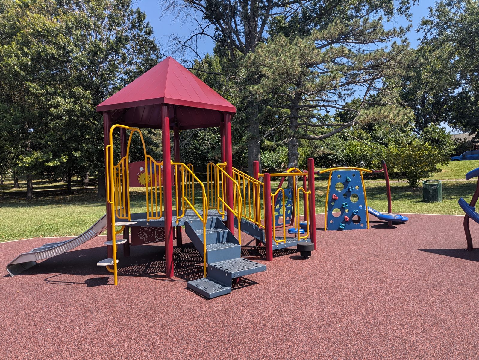 The main play structure at Lindenwood Park in St. Louis, with a red roof, yellow rails, a ramp and a climbing wall on poured rubber surfacing